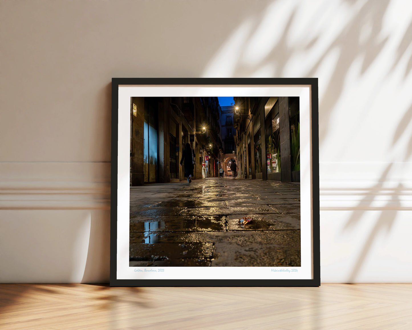 Gasse in Barcelona. Blaue Stunde. Wasserpfütze im Vordergrund. Mehrere Laternen mit Lichterkranz. Vereinzelte Passanten.