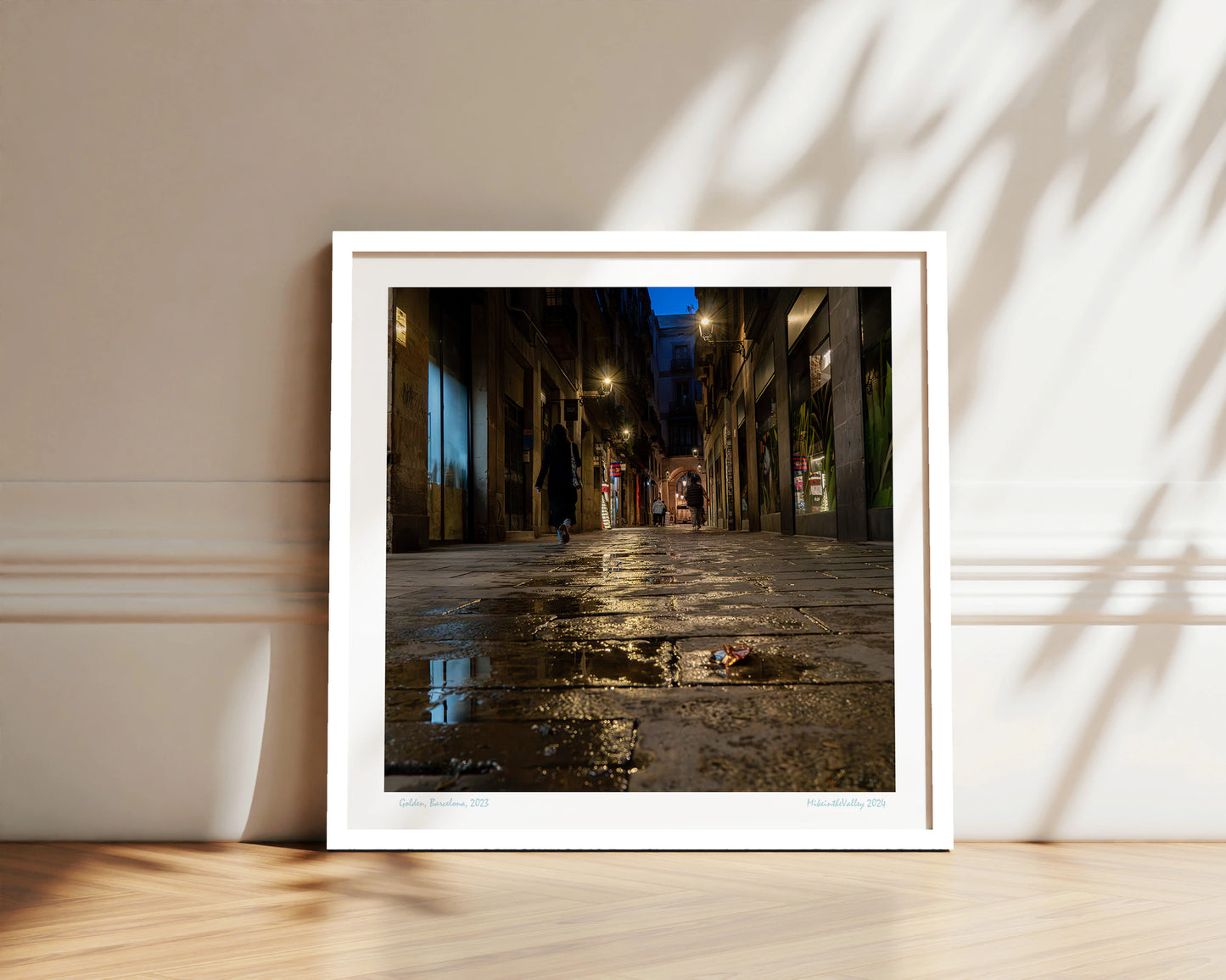 Gasse in Barcelona. Blaue Stunde. Wasserpfütze im Vordergrund. Mehrere Laternen mit Lichterkranz. Vereinzelte Passanten.