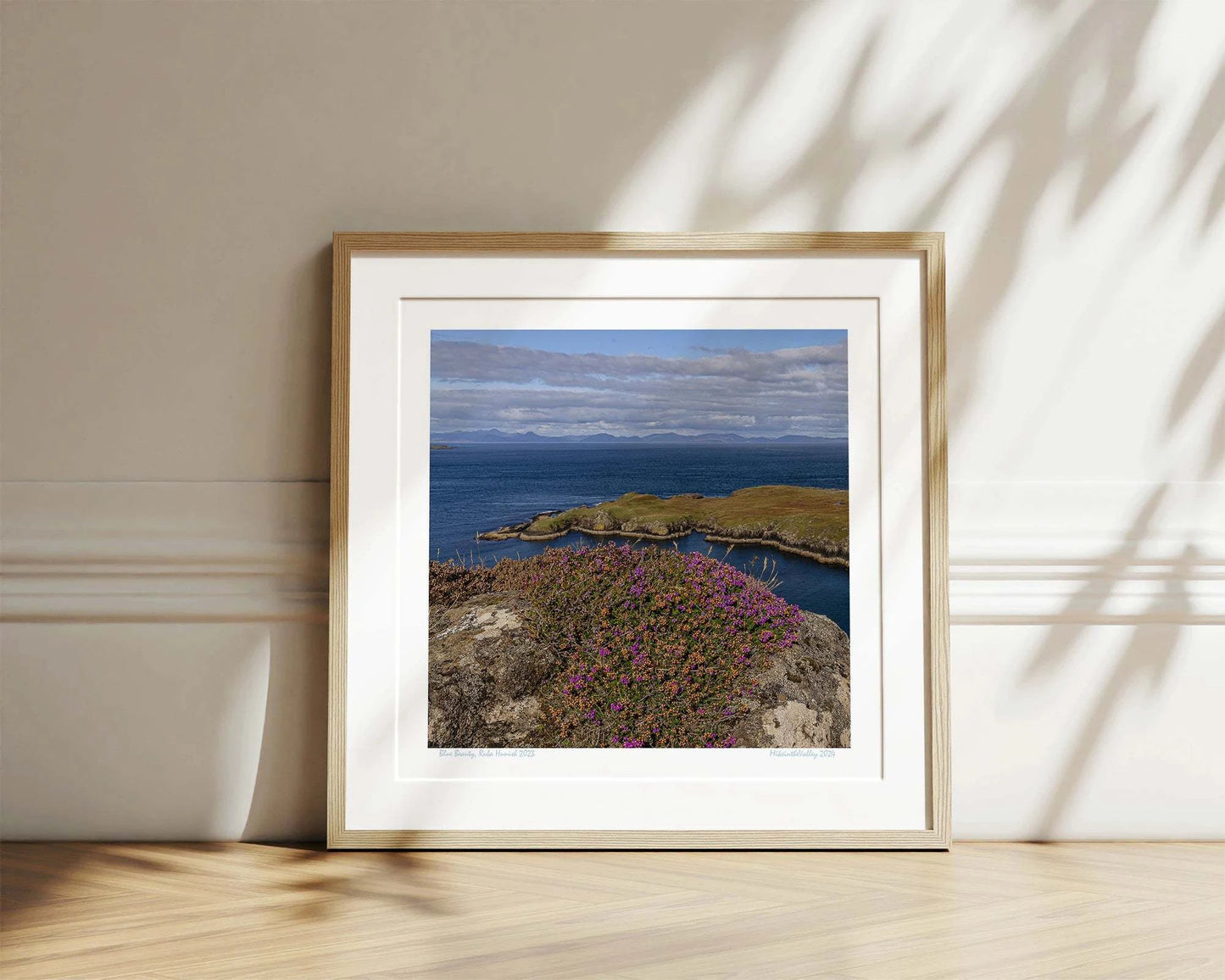 Ein Felsen mit Heidekraut am nördlichsten Ende der Insel Skye in Schottland. Eine Landzunge erstreckt sich quer ins blaue Meer. Im Hintergrund ein Gebirgszug.