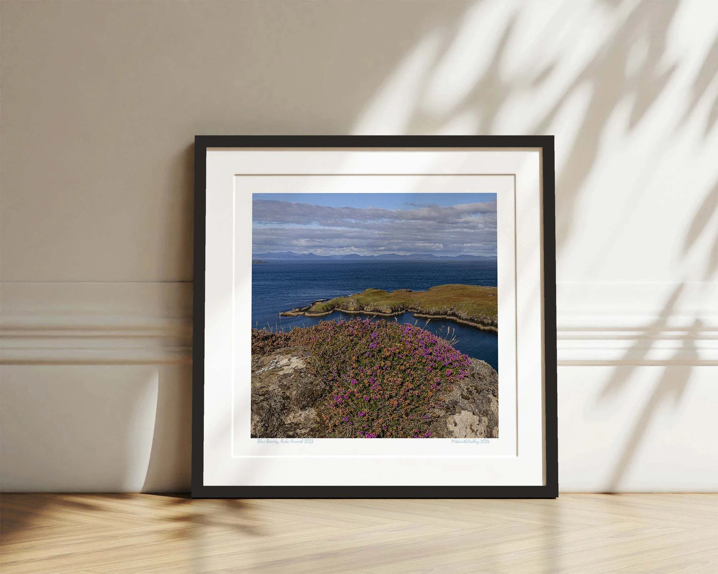 Ein Felsen mit Heidekraut am nördlichsten Ende der Insel Skye in Schottland. Eine Landzunge erstreckt sich quer ins blaue Meer. Im Hintergrund ein Gebirgszug.