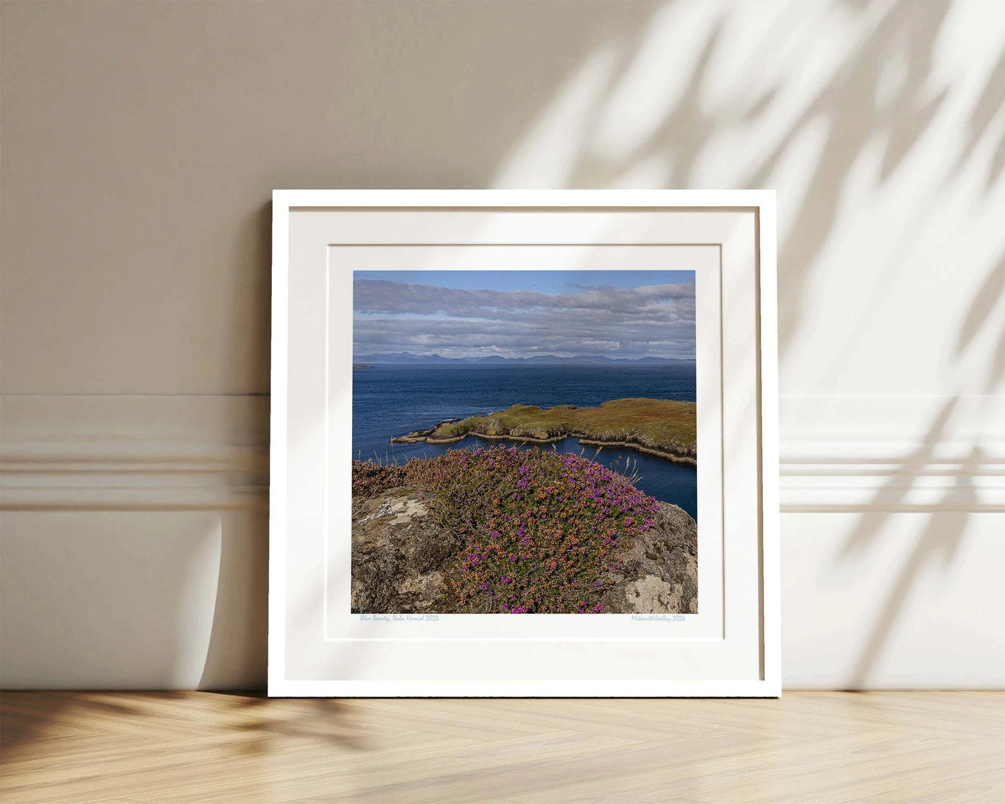 Ein Felsen mit Heidekraut am nördlichsten Ende der Insel Skye in Schottland. Eine Landzunge erstreckt sich quer ins blaue Meer. Im Hintergrund ein Gebirgszug.