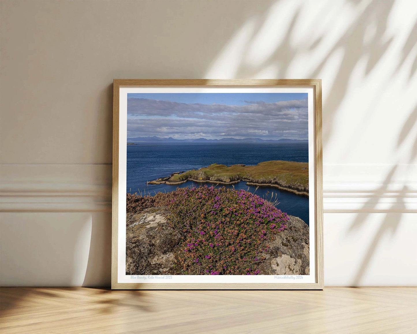 Ein Felsen mit Heidekraut am nördlichsten Ende der Insel Skye in Schottland. Eine Landzunge erstreckt sich quer ins blaue Meer. Im Hintergrund ein Gebirgszug.