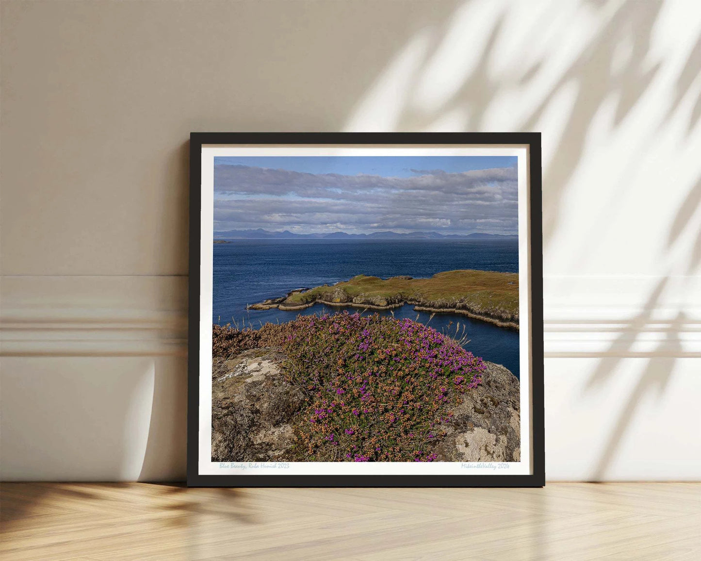 Ein Felsen mit Heidekraut am nördlichsten Ende der Insel Skye in Schottland. Eine Landzunge erstreckt sich quer ins blaue Meer. Im Hintergrund ein Gebirgszug.