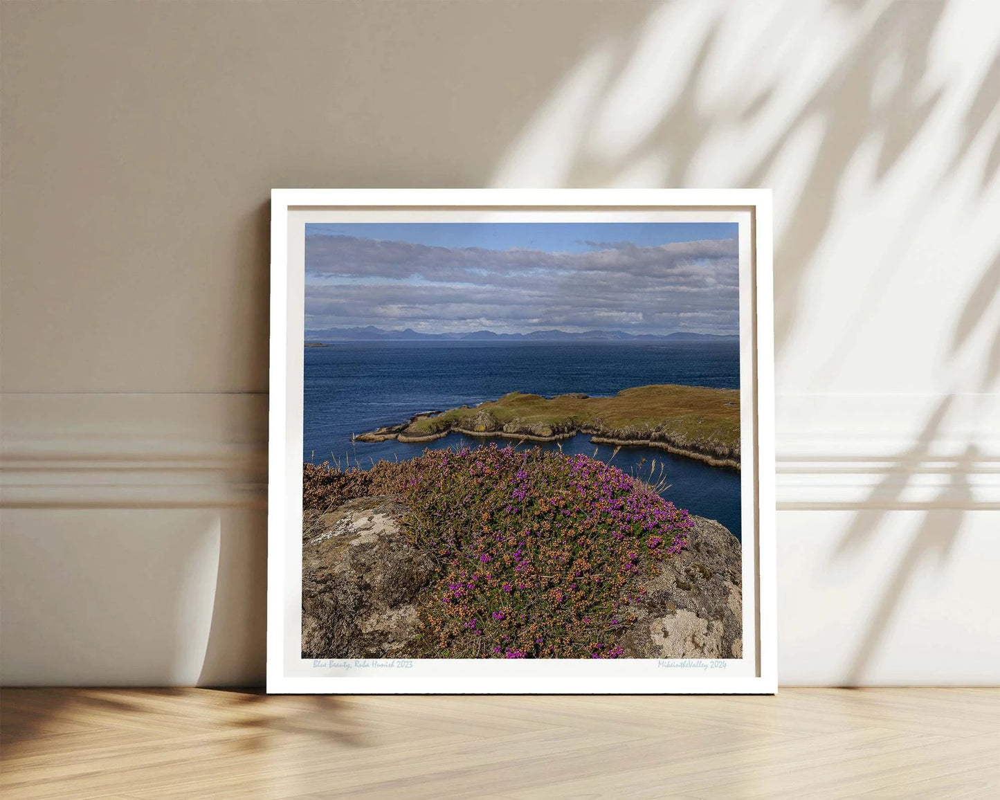 Ein Felsen mit Heidekraut am nördlichsten Ende der Insel Skye in Schottland. Eine Landzunge erstreckt sich quer ins blaue Meer. Im Hintergrund ein Gebirgszug.