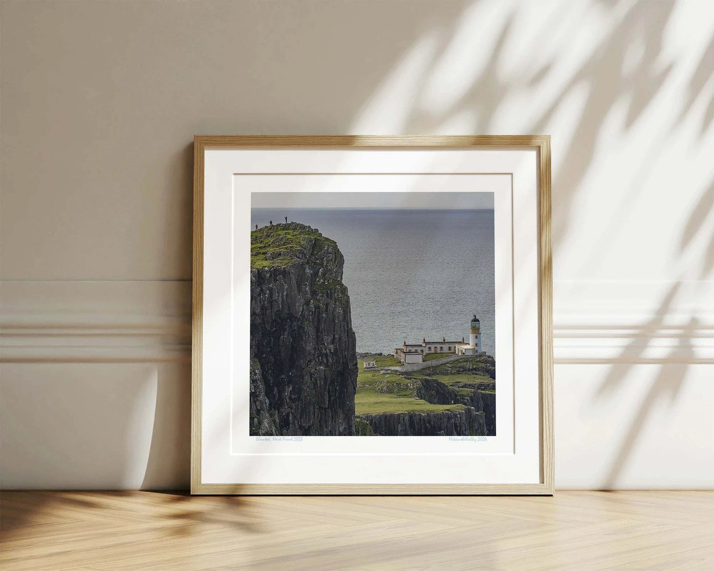 Links im Vordergrund ein riesiger hoher Felsen mit drei winzigen Menschen. Tief darunter der Leuchtturm von Neist Point in den schottischen Highlands.