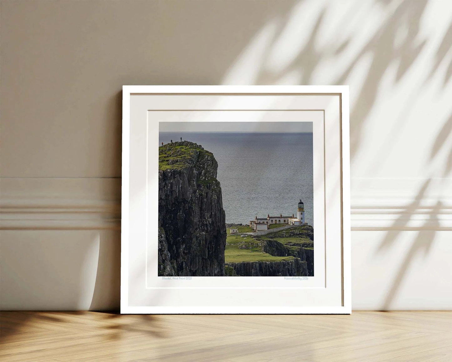 Links im Vordergrund ein riesiger hoher Felsen mit drei winzigen Menschen. Tief darunter der Leuchtturm von Neist Point in den schottischen Highlands.