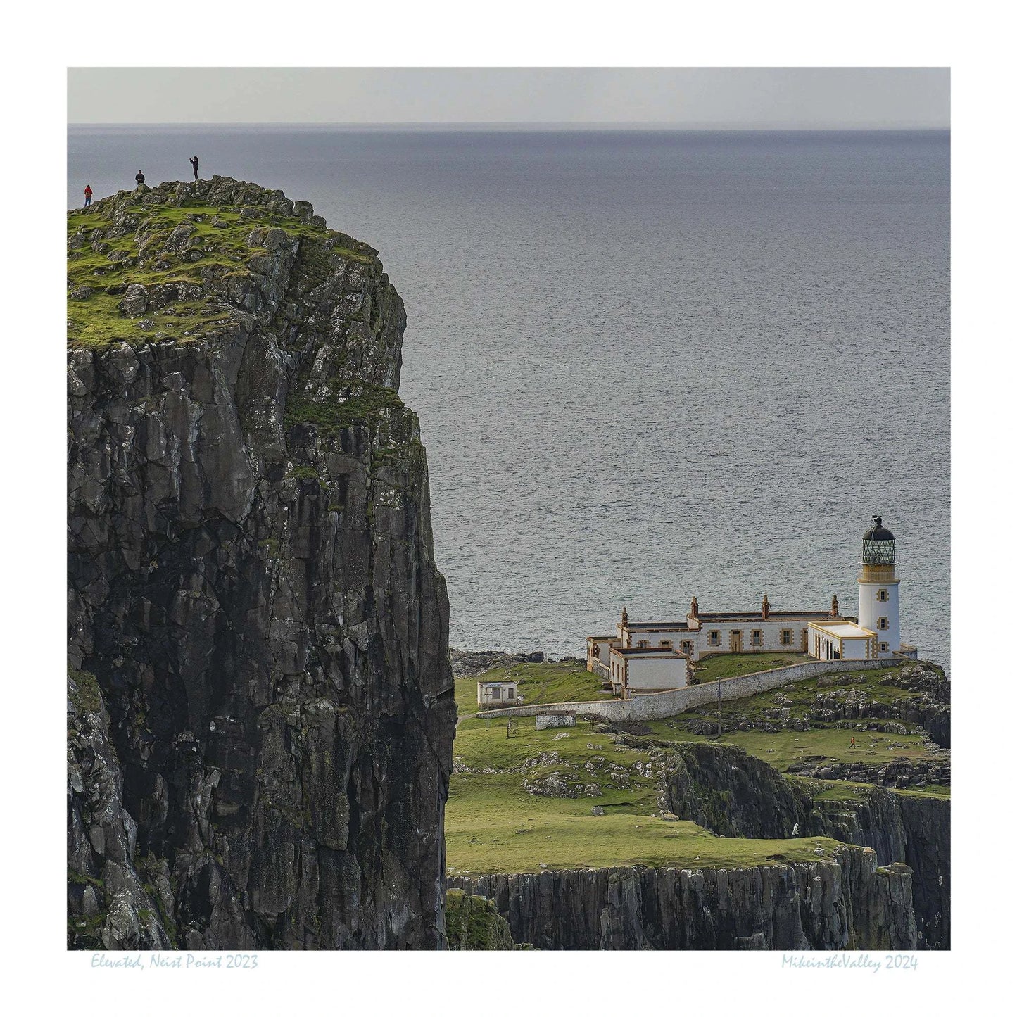 Links im Vordergrund ein riesiger hoher Felsen mit drei winzigen Menschen. Tief darunter der Leuchtturm von Neist Point in den schottischen Highlands.