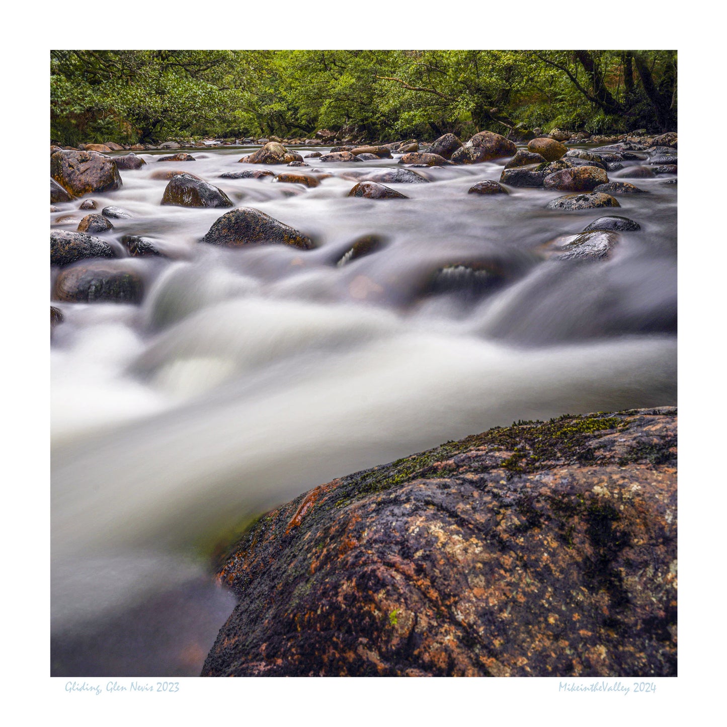 Wie traumhafter Nebel fließt der Fluss Nevis zwischen den riesigen Kieselsteinen im Flussbett. Im Hintergrund urige Laubbäume.