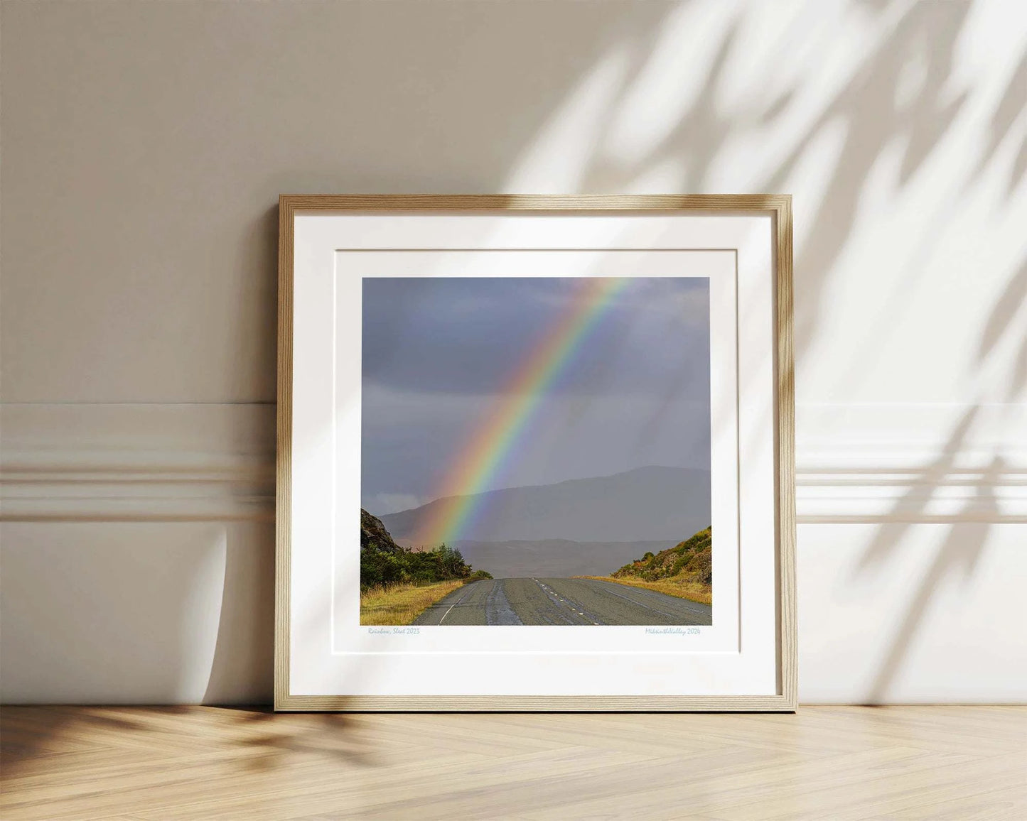 Ein kräftiger Regenbogen erhebt sich über eine Straße im Süden der Insel Skye in Schottland. Im Hintergrund eine Bergkette.