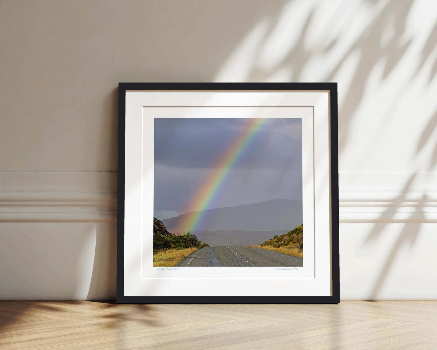 Ein kräftiger Regenbogen erhebt sich über eine Straße im Süden der Insel Skye in Schottland. Im Hintergrund eine Bergkette.