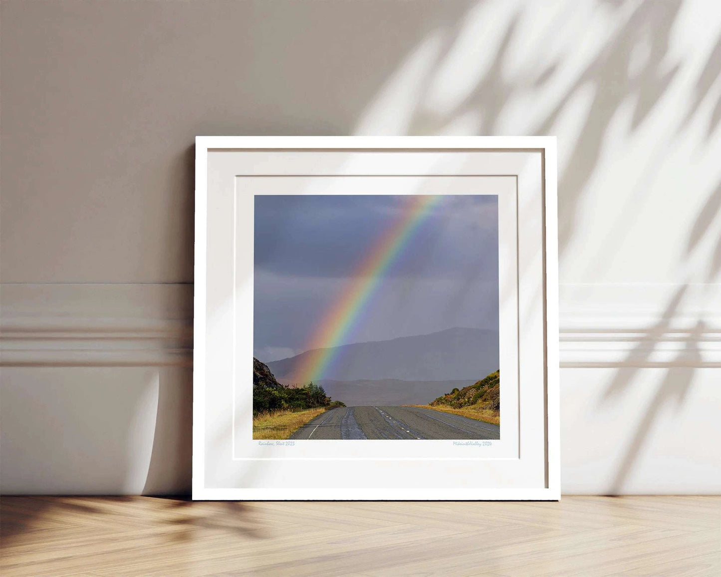 Ein kräftiger Regenbogen erhebt sich über eine Straße im Süden der Insel Skye in Schottland. Im Hintergrund eine Bergkette.