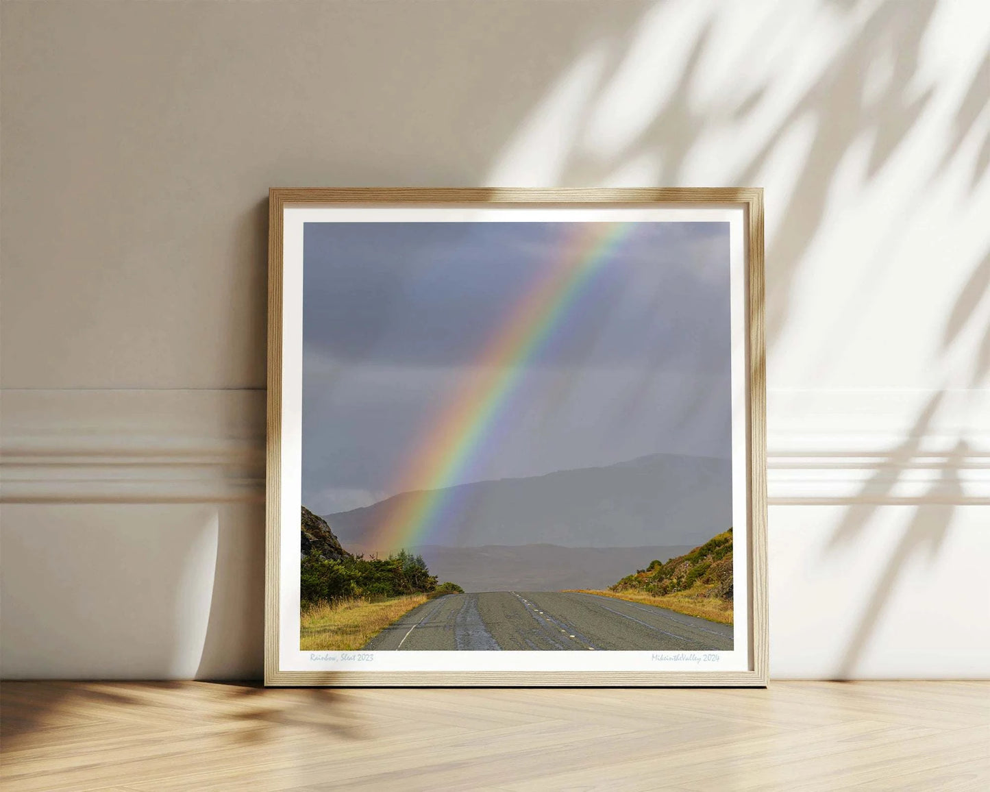 Ein kräftiger Regenbogen erhebt sich über eine Straße im Süden der Insel Skye in Schottland. Im Hintergrund eine Bergkette.