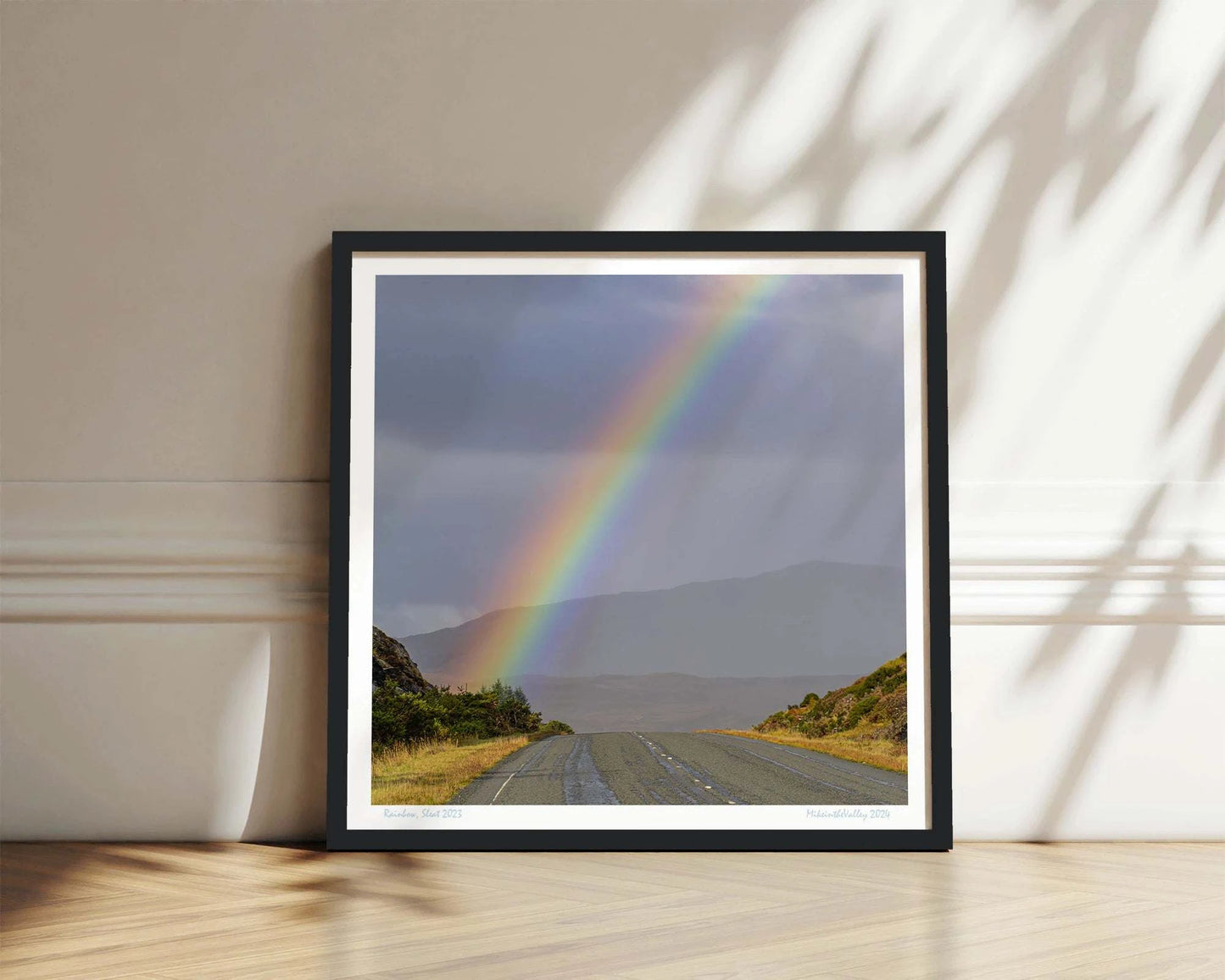 Ein kräftiger Regenbogen erhebt sich über eine Straße im Süden der Insel Skye in Schottland. Im Hintergrund eine Bergkette.