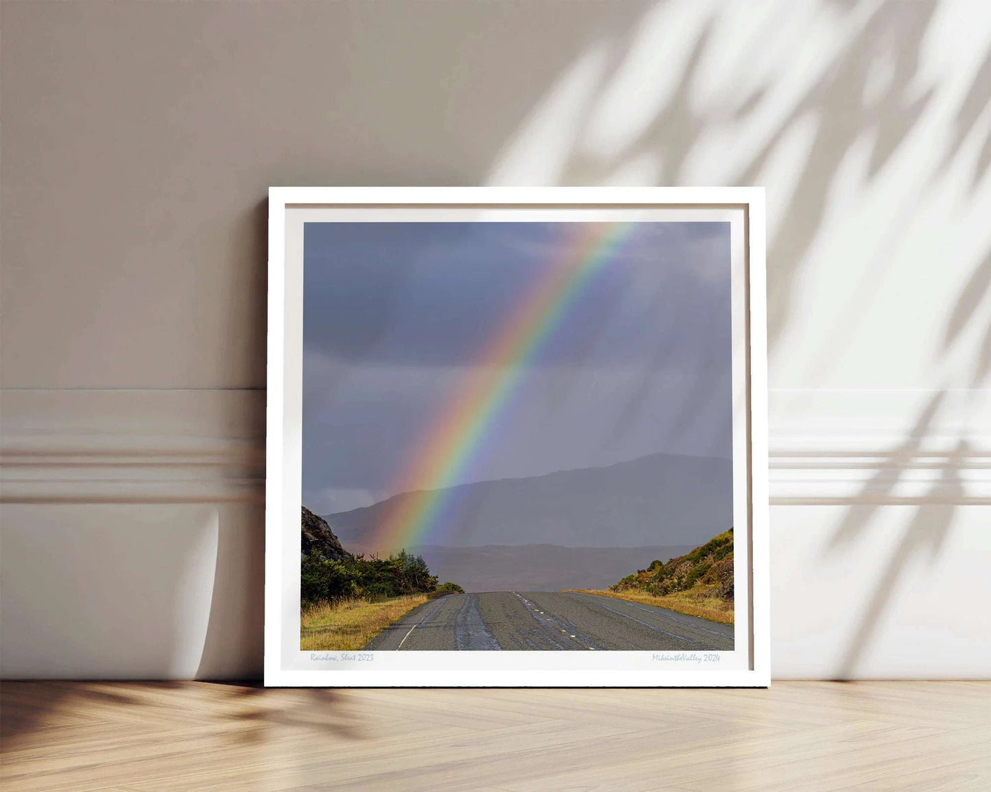 Ein kräftiger Regenbogen erhebt sich über eine Straße im Süden der Insel Skye in Schottland. Im Hintergrund eine Bergkette.