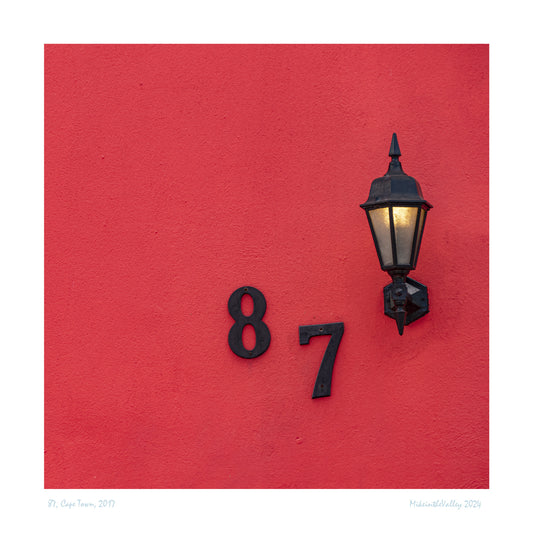 Nahaufnahme rote Hauswand mit leuchtender Laterne und der Hausnummer 87. Laterne und Hausnummer aus Gußeisen.
